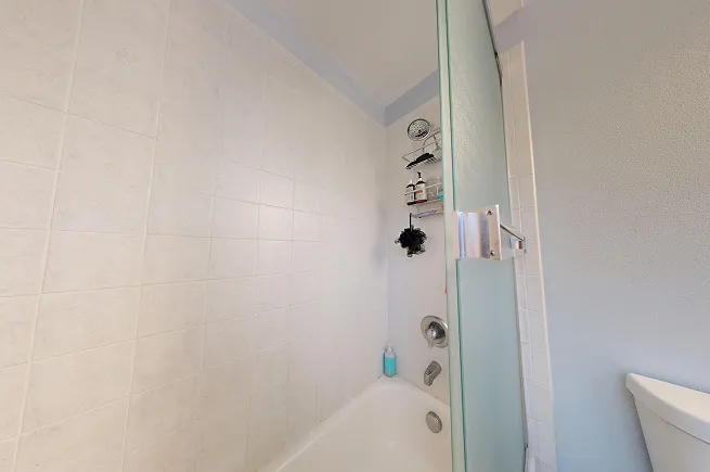 Interior of original tub-shower with white tile surround and chrome fixtures before demolition and microcement conversion.