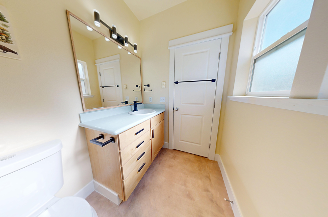 Refreshed bathroom vanity with light oak cabinet, microcement countertop, matte black hardware, and updated vanity light fixture.