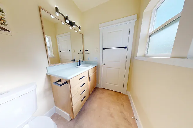 Refreshed bathroom vanity with light oak cabinet, microcement countertop, matte black hardware, and updated vanity light fixture.