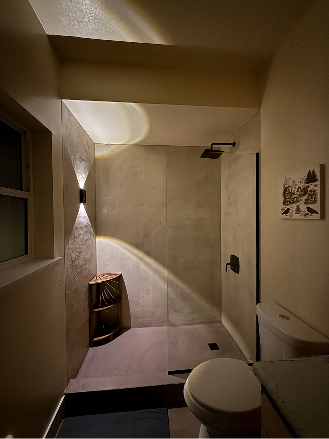 West Seattle microcement shower at night with warm wall sconce lighting highlighting the texture and tone of the finished walls.