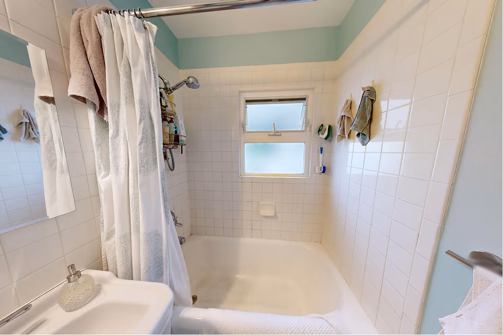Original 1928 Capitol Hill bathroom with cast-iron tub, shower curtain, and window inside the tub surround before remodel