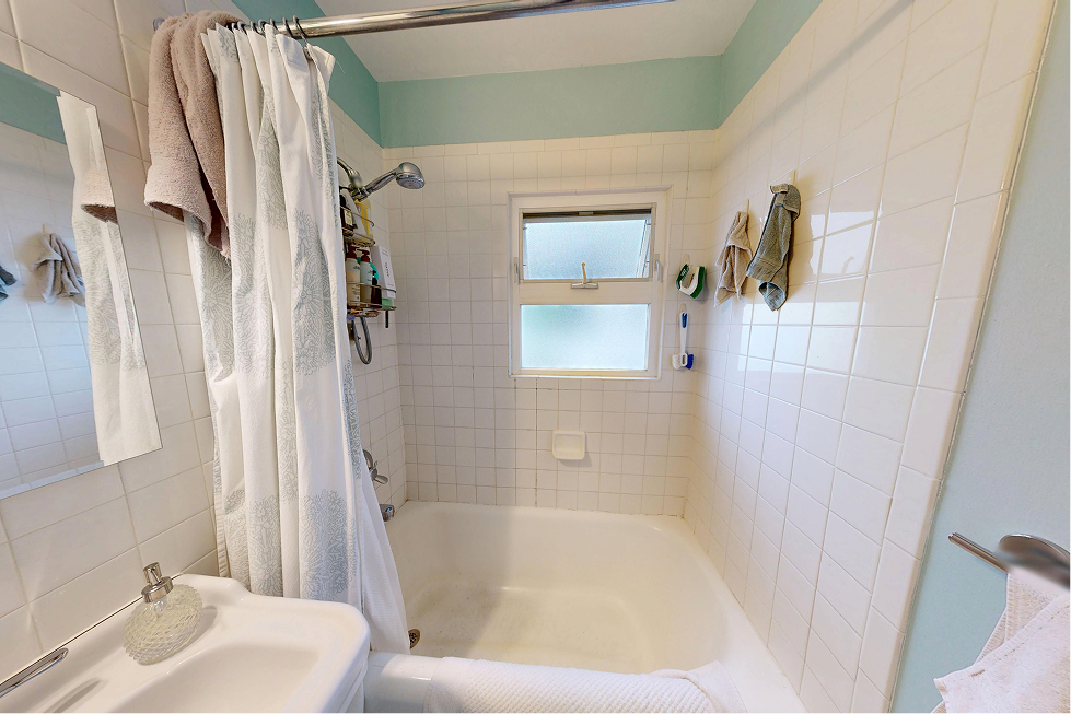 Original 1928 Capitol Hill bathroom with cast-iron tub, shower curtain, and window inside the tub surround before renovation