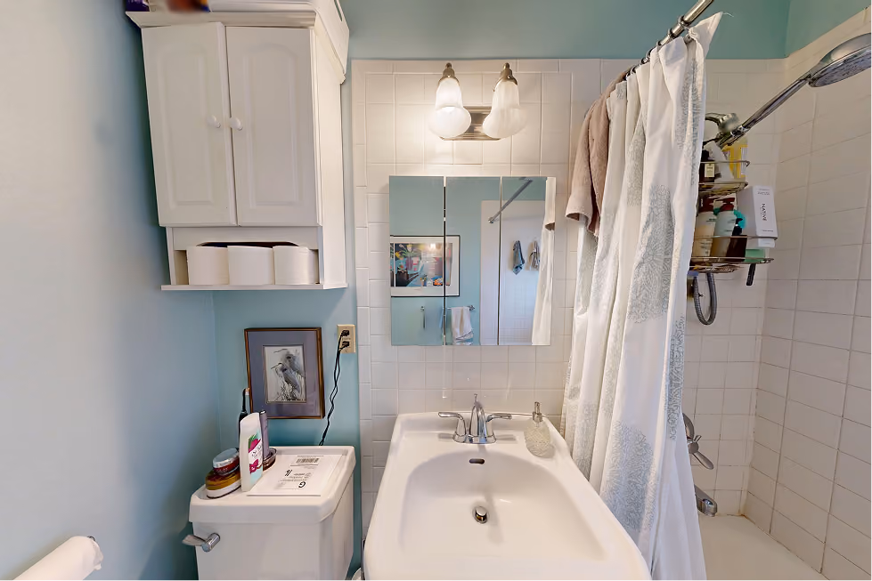 Dated tub and shower with small white tile, chrome fixtures, and hanging shower caddy before Seattle bathroom remodel