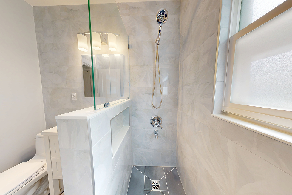 Walk-in shower with tiled niche, pony wall, handheld chrome shower head, and large-format marble-look tile