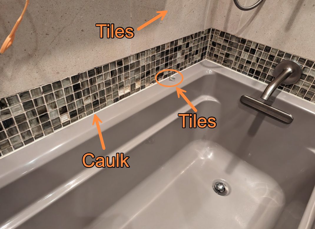 Tub surround with arrows labelling the mosaic tile field and the caulk joint at the tub edge.