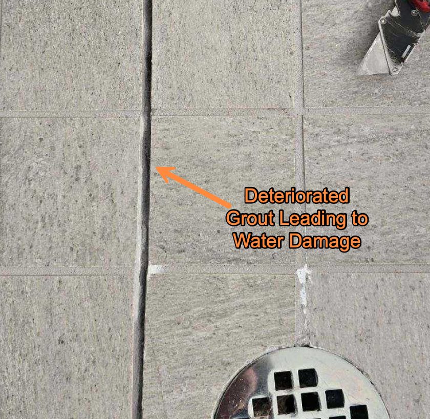 Close-up of shower floor tile with an arrow marking deteriorated grout leading to water damage.