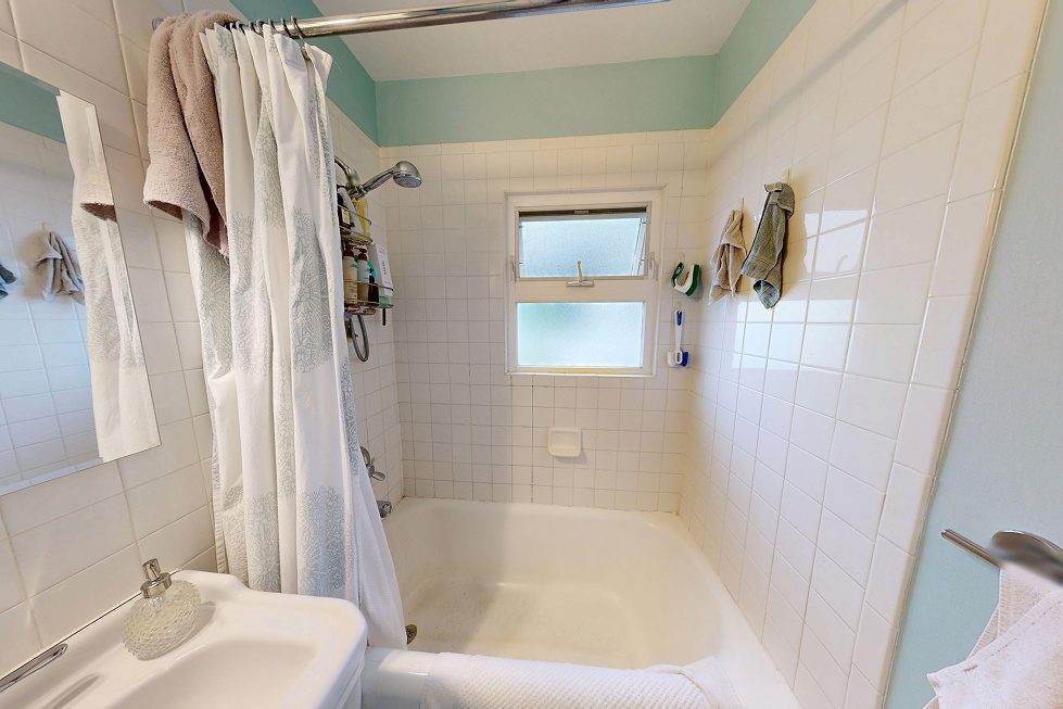 Original 1928 Capitol Hill bathroom with cast-iron tub, shower curtain, and window inside the tub surround before renovation