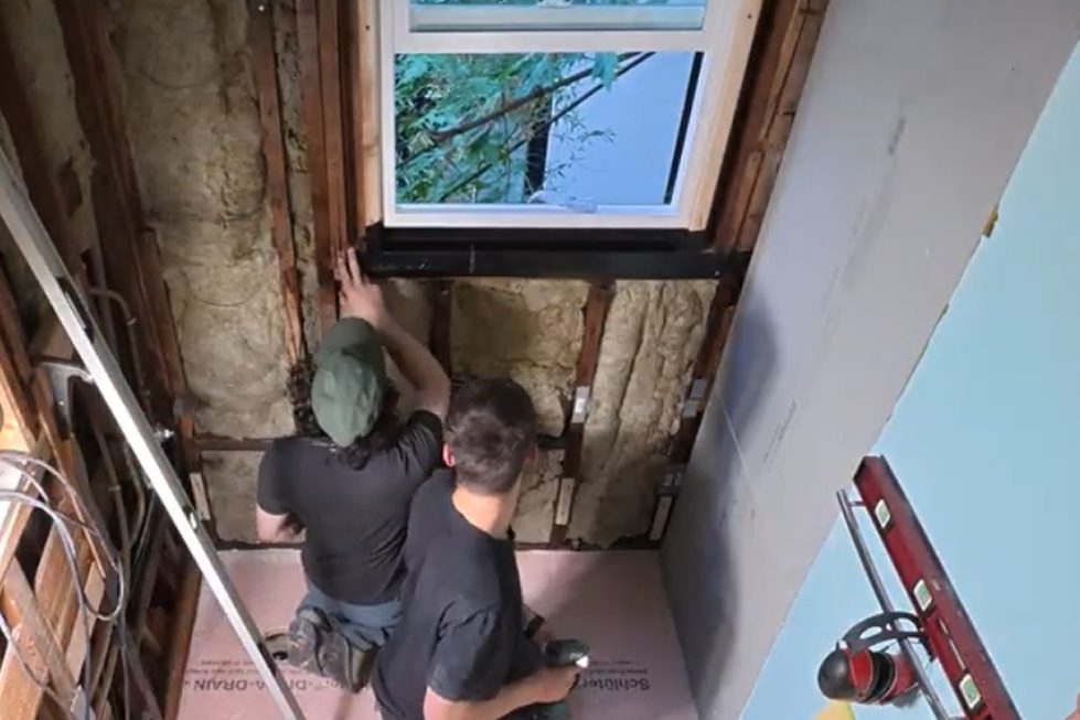 Two DuetRight crew members rebuilding a second-floor bathroom window opening down to the framing.