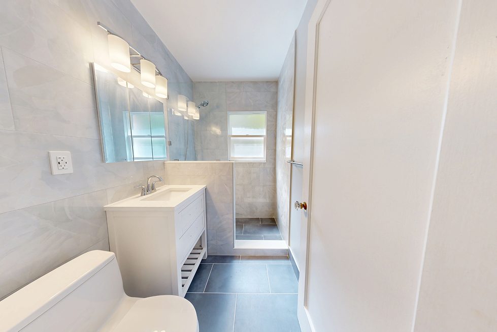 Renovated Seattle bathroom with white vanity, walk-in shower, marble-look wall tile, and slate-blue porcelain floor