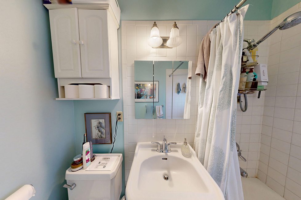 Dated tub and shower with small white tile, chrome fixtures, and hanging shower caddy before Seattle bathroom renovation