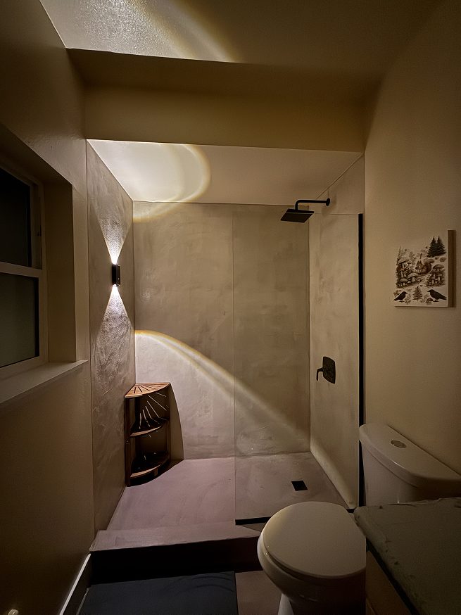 West Seattle microcement shower at night with warm wall sconce lighting highlighting the texture and tone of the finished walls.
