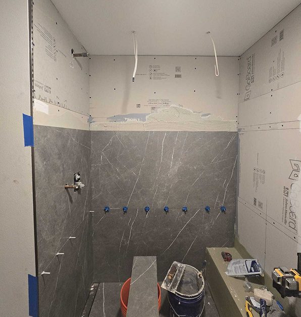 A shower mid-renovation, showing large gray tiles being installed over a waterproof backer board system.