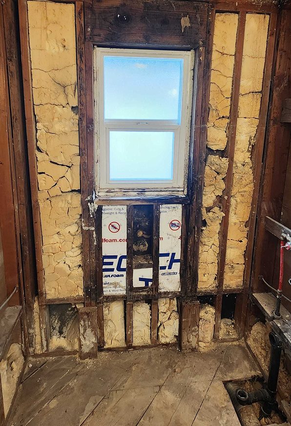 Shower walls taken down to the studs during a bathroom demolition, exposing framing and insulation around a window.