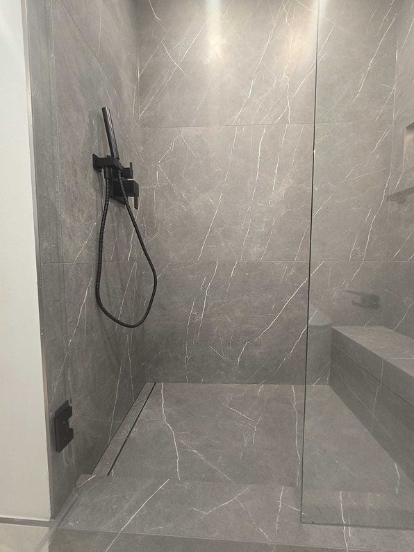 Modern walk-in shower with large gray porcelain tiles, a built-in bench, and a sleek black linear drain.