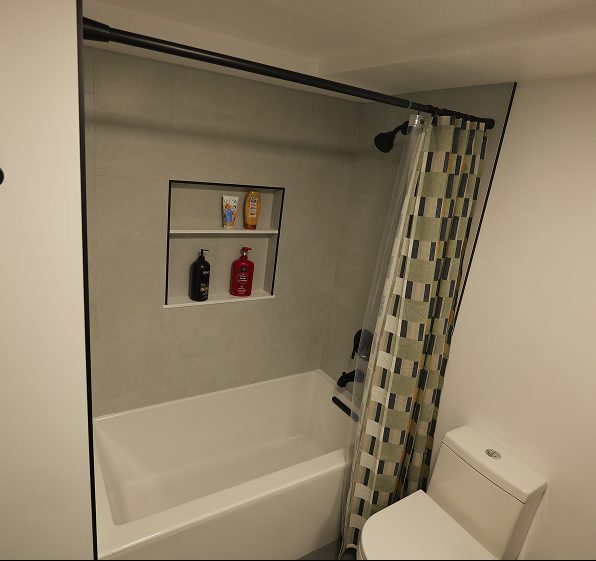 A new bathtub and shower with a custom-built, recessed tile niche for storing shampoo and soap bottles.
