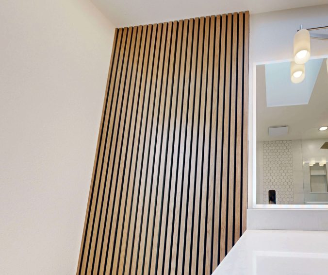 Vertical light oak slat wall panel beside a bathroom mirror and pendant light.