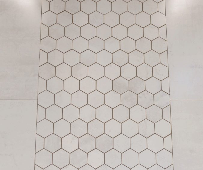 White hexagon mosaic accent tile set against large-format wall tile.