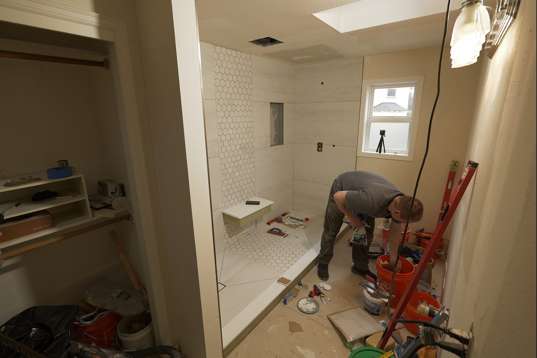 Renovation in progress: white subway tile going up in the shower while a crew member works on the floor.