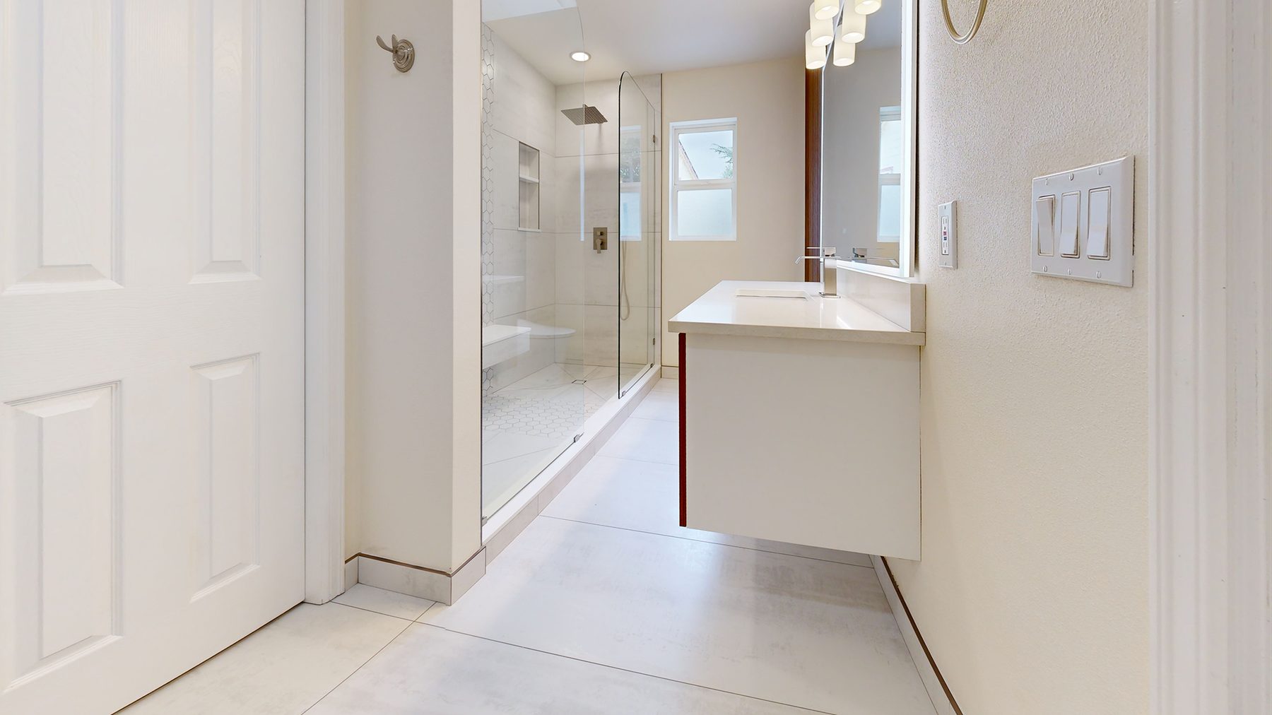 After: view from the hallway into the finished bathroom, showing the floating vanity, lit mirror, and tile floor.