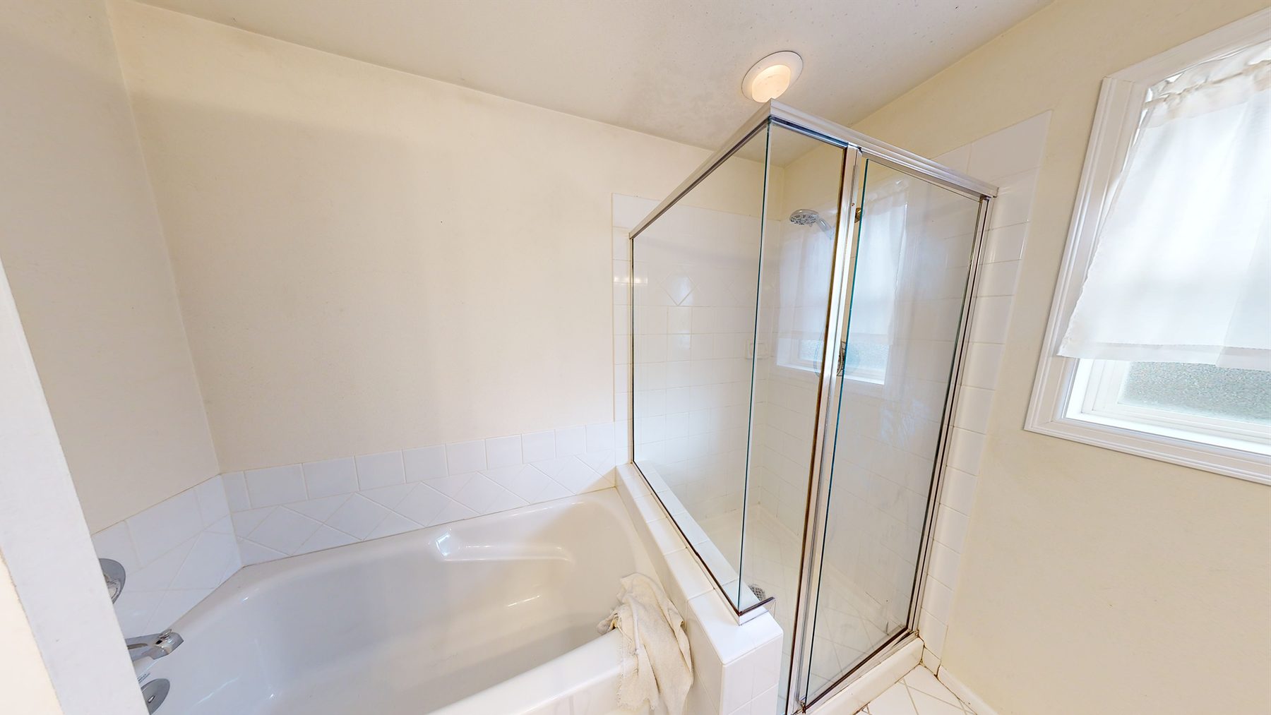 Before: original alcove tub with a glass panel, beige tile, and a skylight above.
