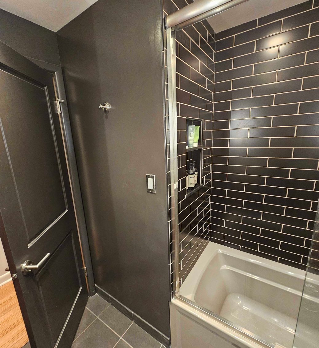 Finished shower in charcoal subway tile with a mosaic accent band and a glass panel.