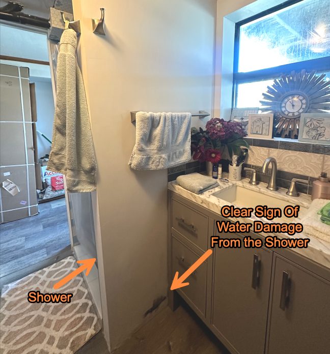 Bathroom vanity and floor with arrows marking water damage spreading from the shower.