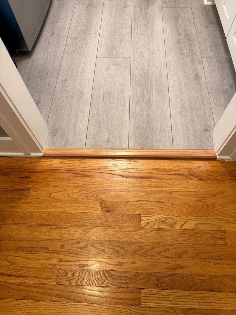 Grey-toned plank flooring meeting original oak hardwood at the kitchen threshold