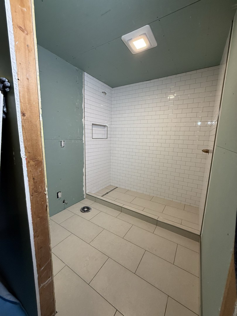 Subway tile in running bond meeting the shower curb and floor tile, with a niche framed into the back wall