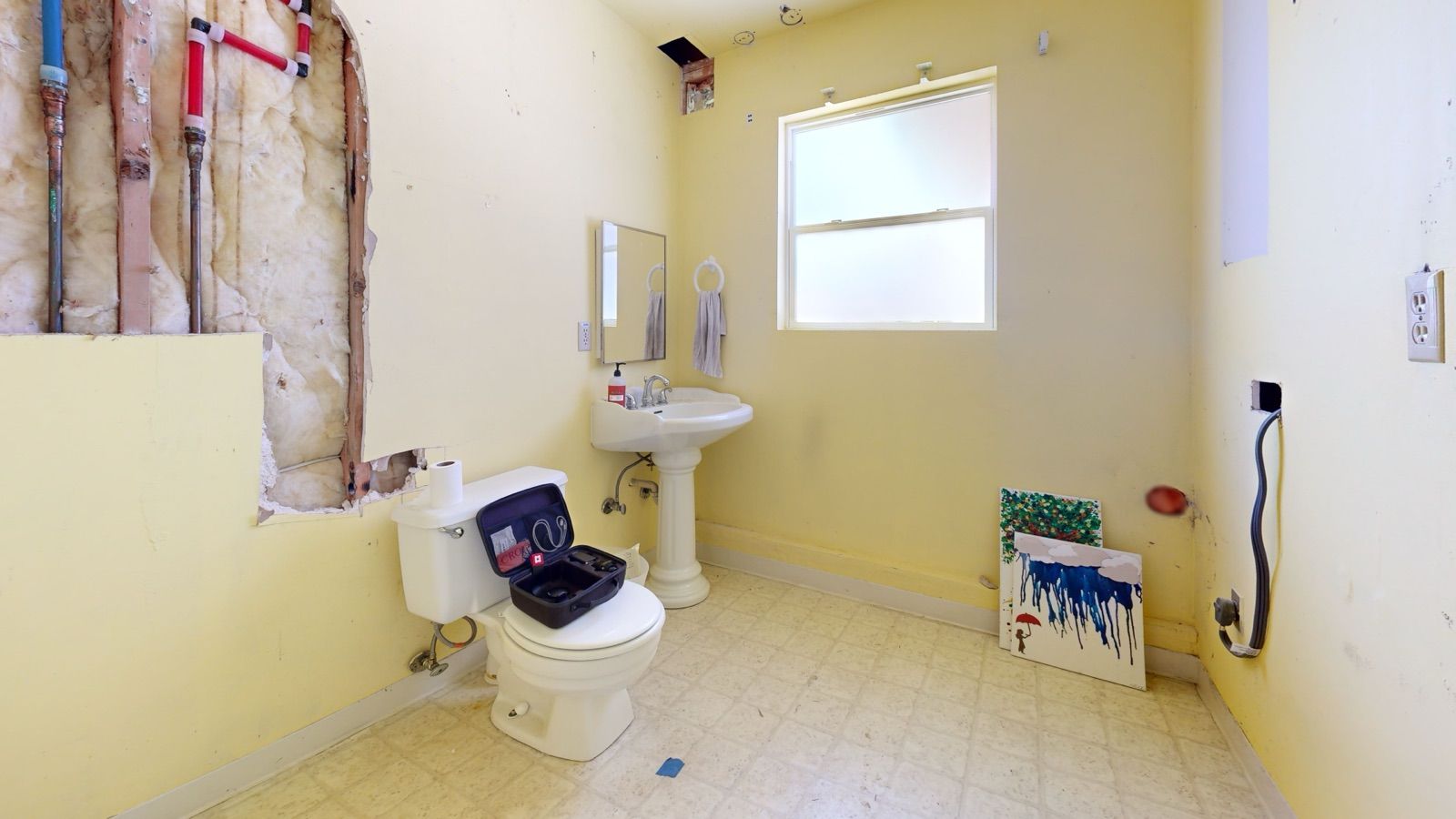 West Seattle basement bathroom before renovation, with open walls, exposed plumbing, yellow paint and a vinyl floor