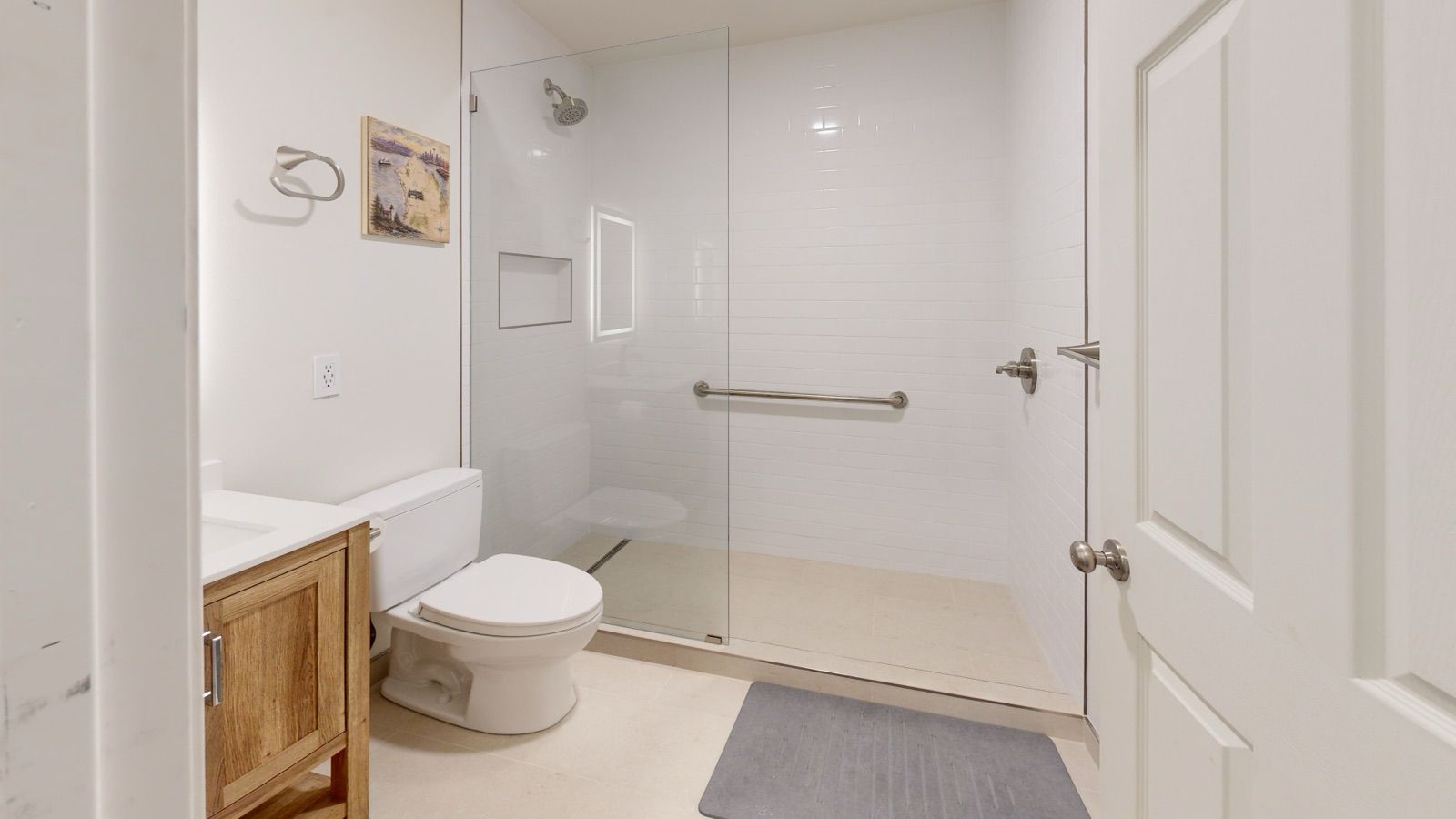 Finished basement bathroom with a white subway tile walk-in shower, fixed glass panel, grab bar and linear drain