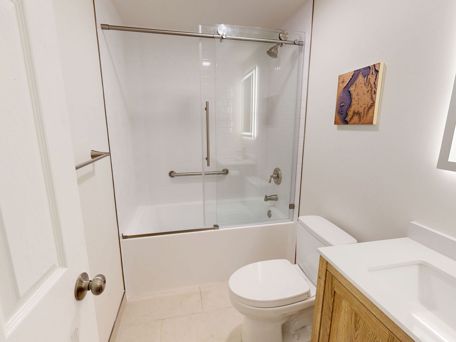 Renovated guest bathroom with a white subway tile tub surround, sliding glass tub door, grab bars and a wood vanity