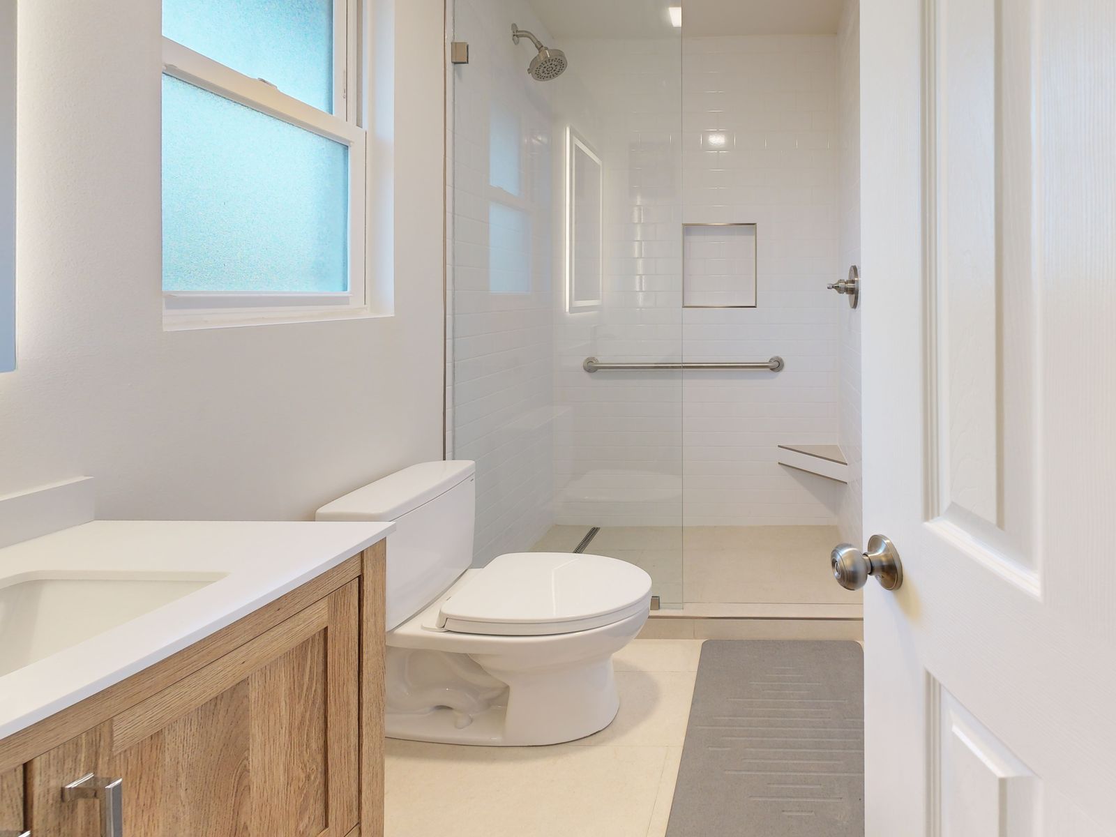 Renovated master bathroom with a walk-in shower, recessed niche, grab bar and wood vanity