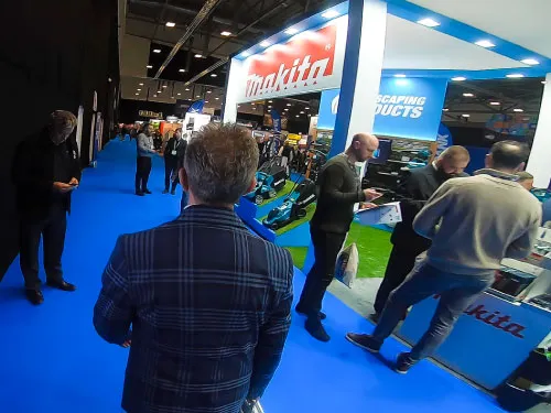 People viewing equipment at a Makita booth with blue carpet in an indoor trade show or exhibition.