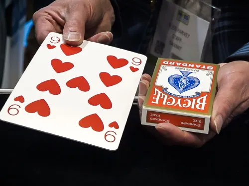 Hands holding a large nine of hearts card and a Bicycle standard playing cards box.