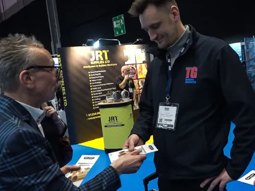 Two men exchanging business cards at a trade show booth with JRT Supplies branding.
