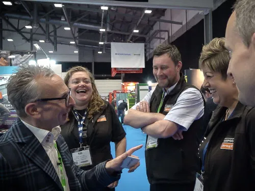 Five people in conversation at an indoor event, smiling and engaging warmly with each other.