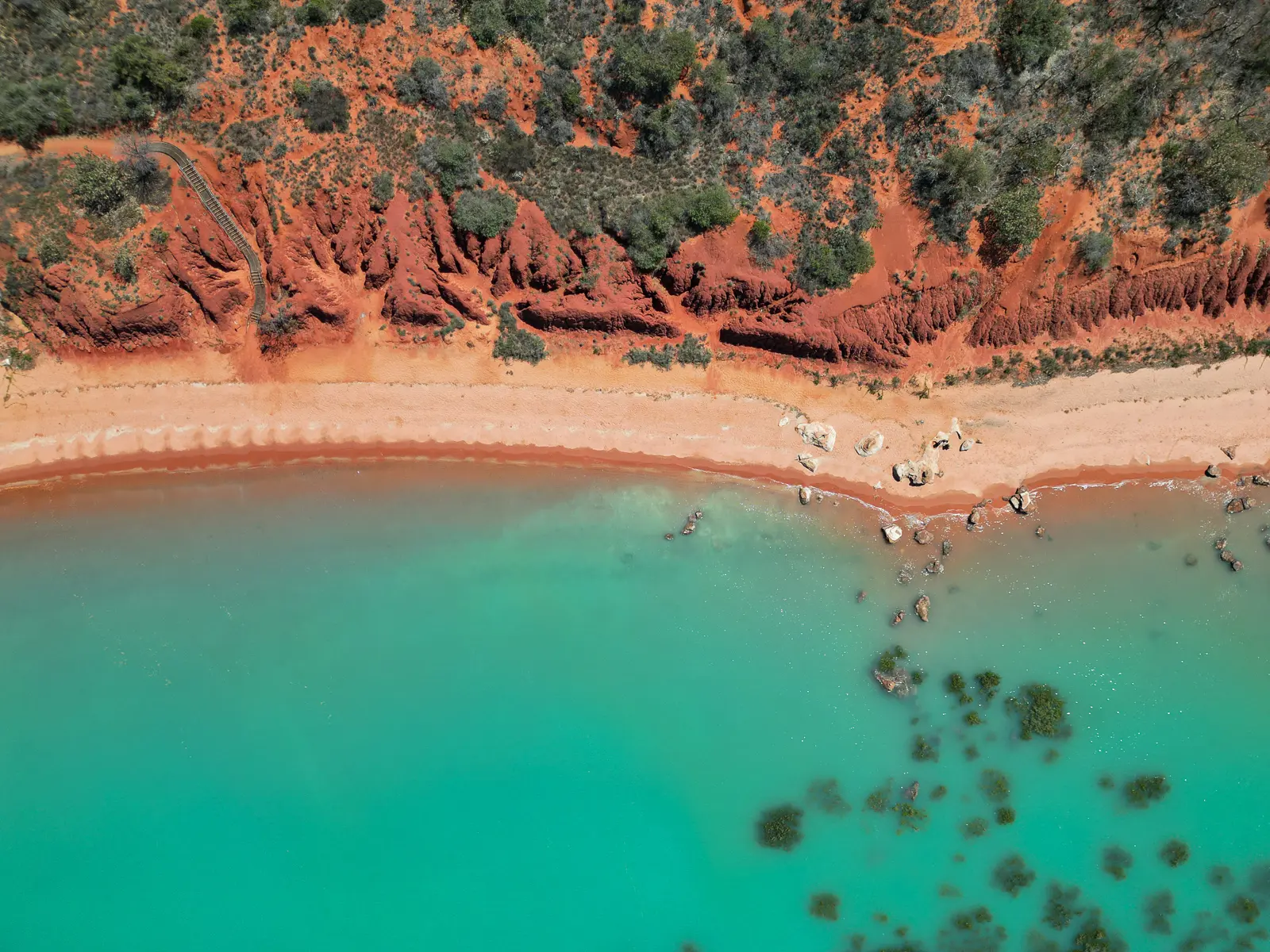 Aerial view of turquoise water meeting red coastal cliffs near Broome, Western Australia