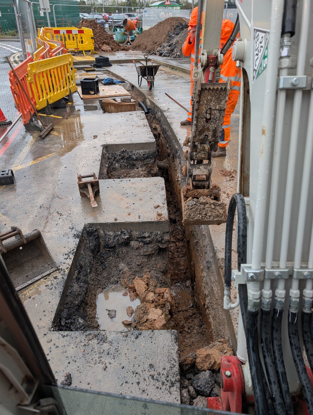 Trench excavation through a commercial forecourt behind safety barriers