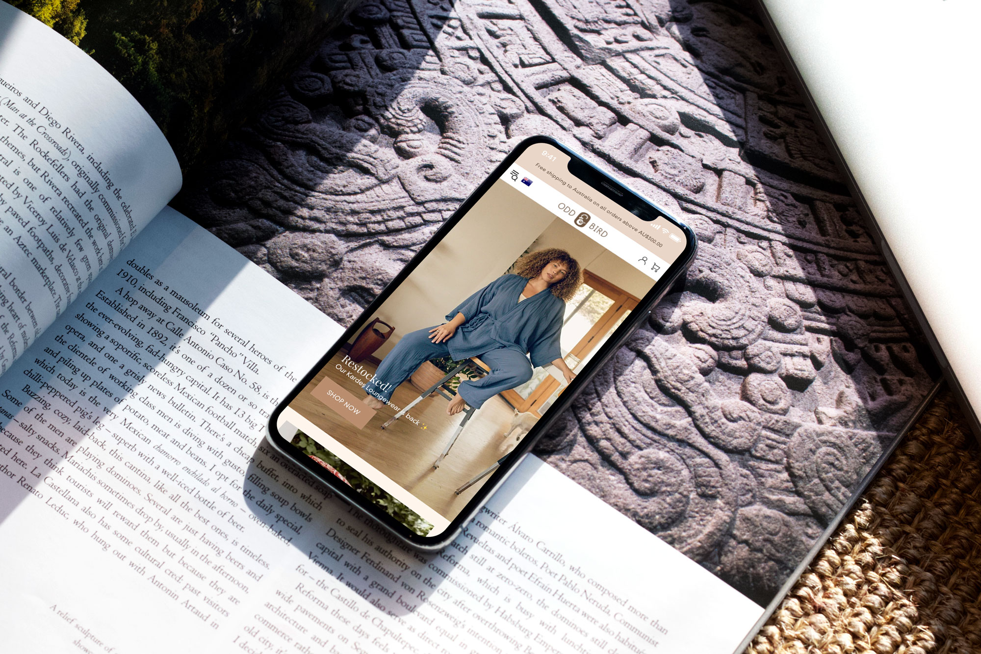 The Oddbird site on a phone resting on a knitted blanket beside an open book
