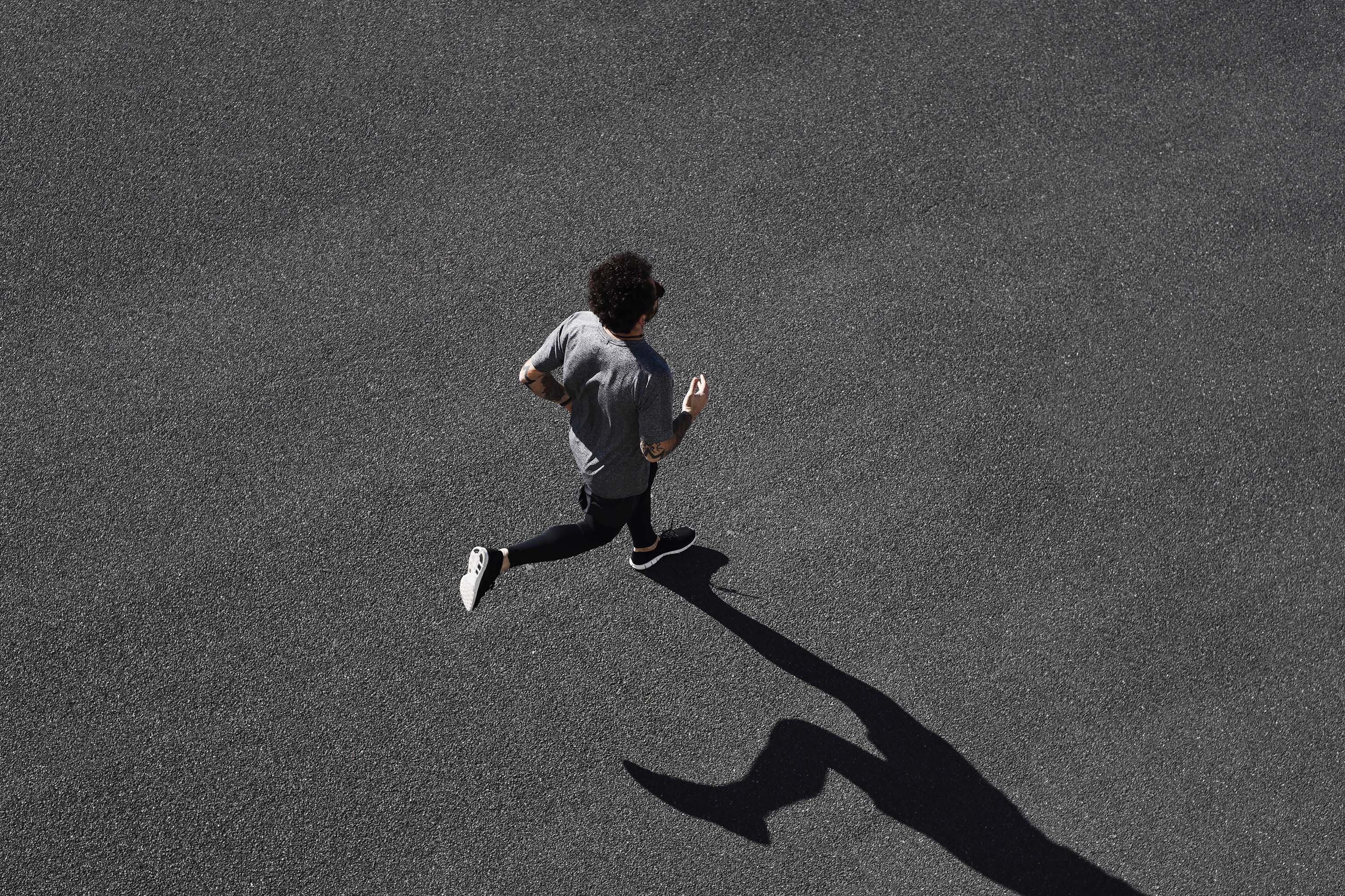 Overhead view of a man running along the road surrounded by his shadow.
