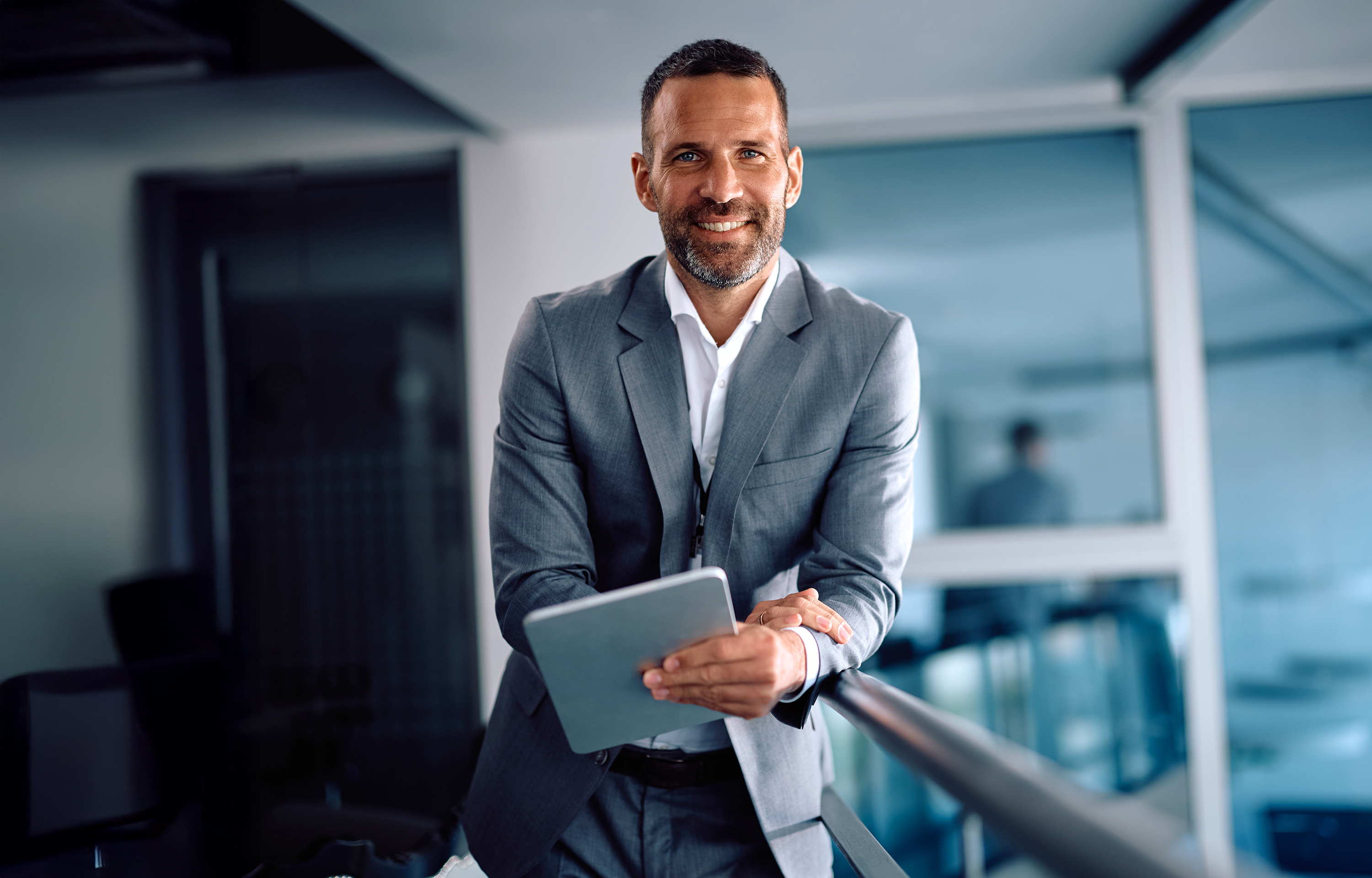 A man in a suit holding a tablet computer, looking focused and engaged in a professional setting.