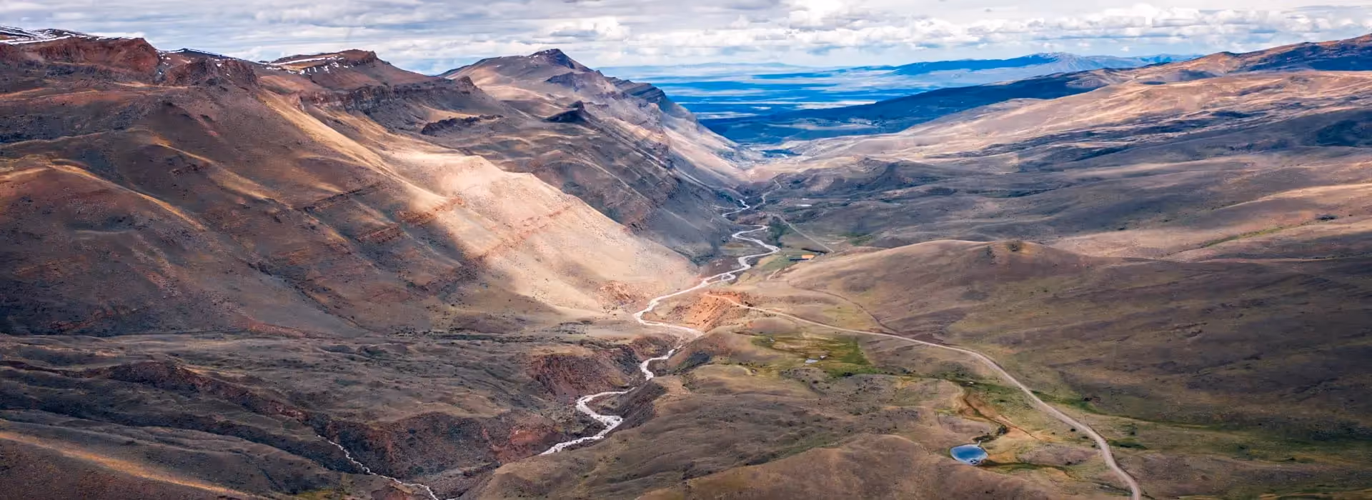 A winding river and road cut through a broad mountain valley beneath a cloudy sky in Patagonia.