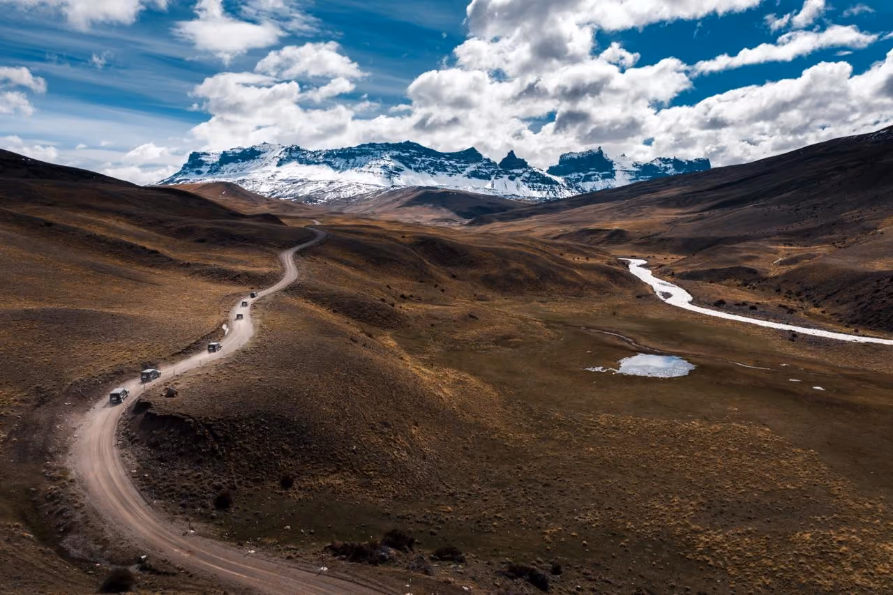 Convoy of 4WD vehicles travelling through a mountain valley towards snow-covered peaks in Patagonia.