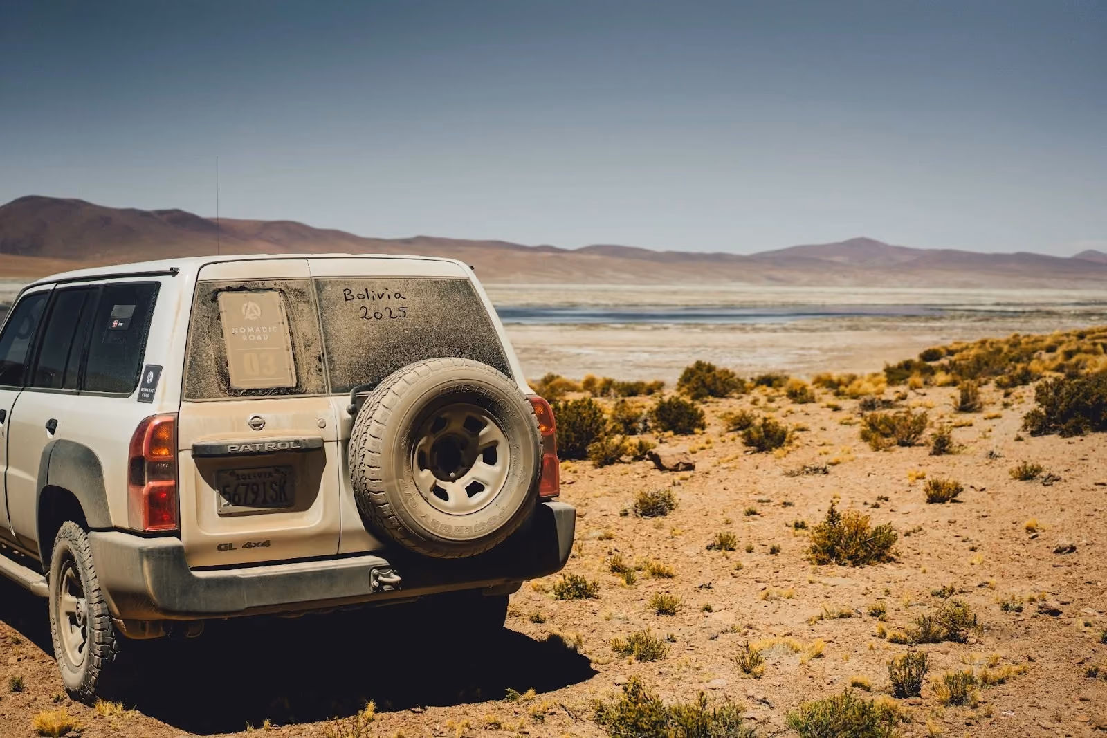 Dusty Nomadic Road 4WD vehicle overlooking a salt lagoon in Bolivia's Altiplano.