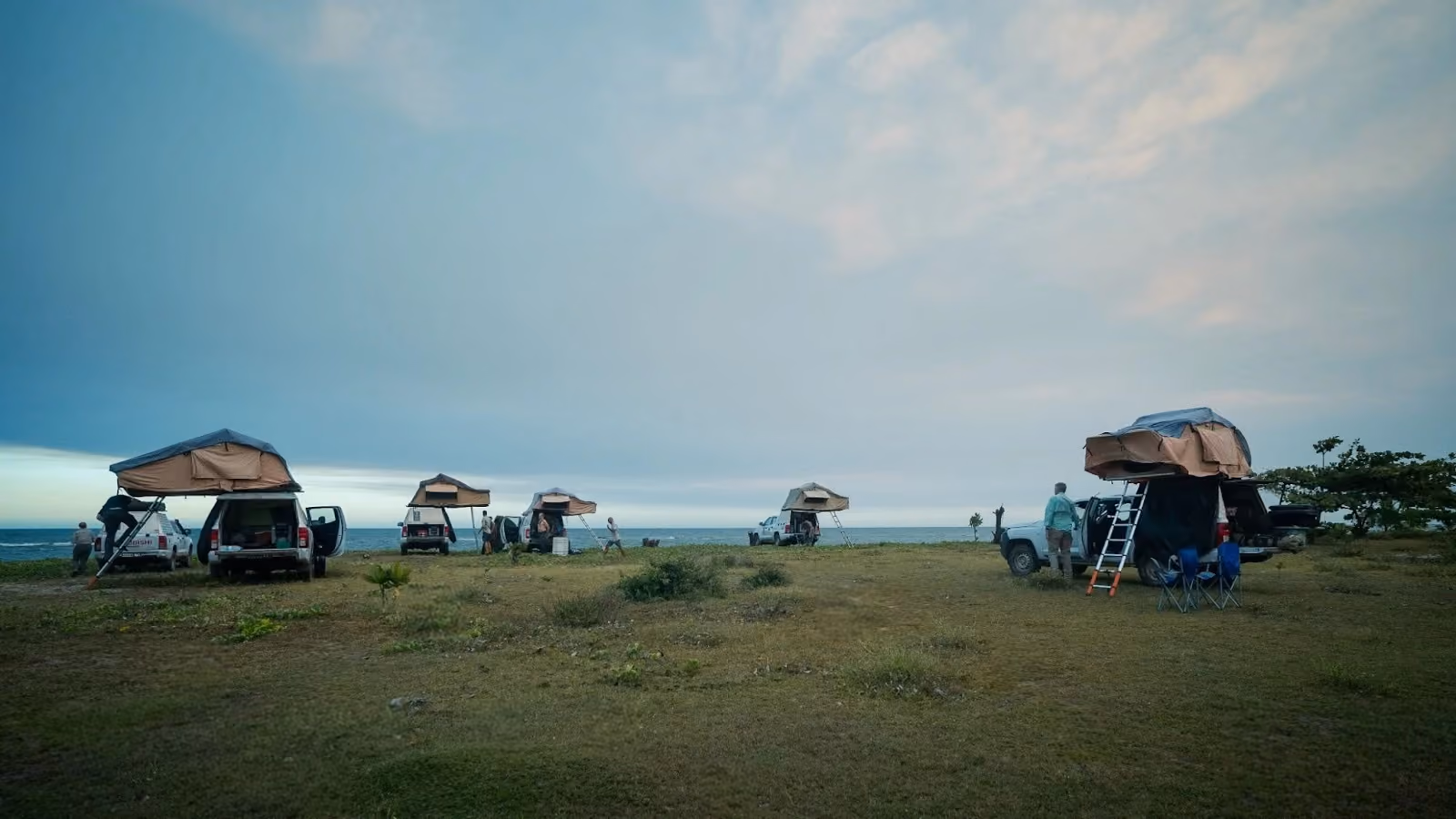 4WD vehicles with rooftop tents at a remote coastal campsite.