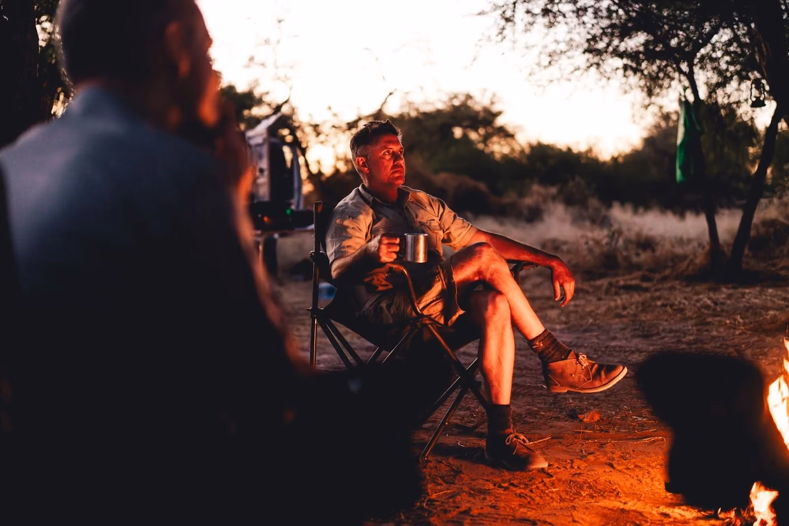 Traveller sitting beside a campfire at dusk in a remote safari camp.