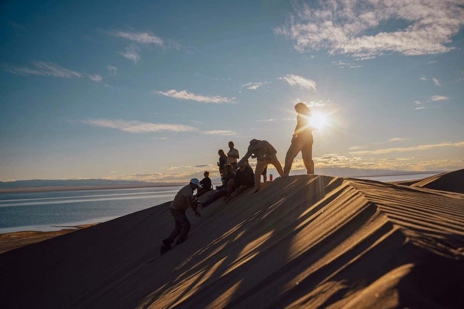 Travellers climbing the Mongol Els sand dunes beside Lake Dorgon at sunset.