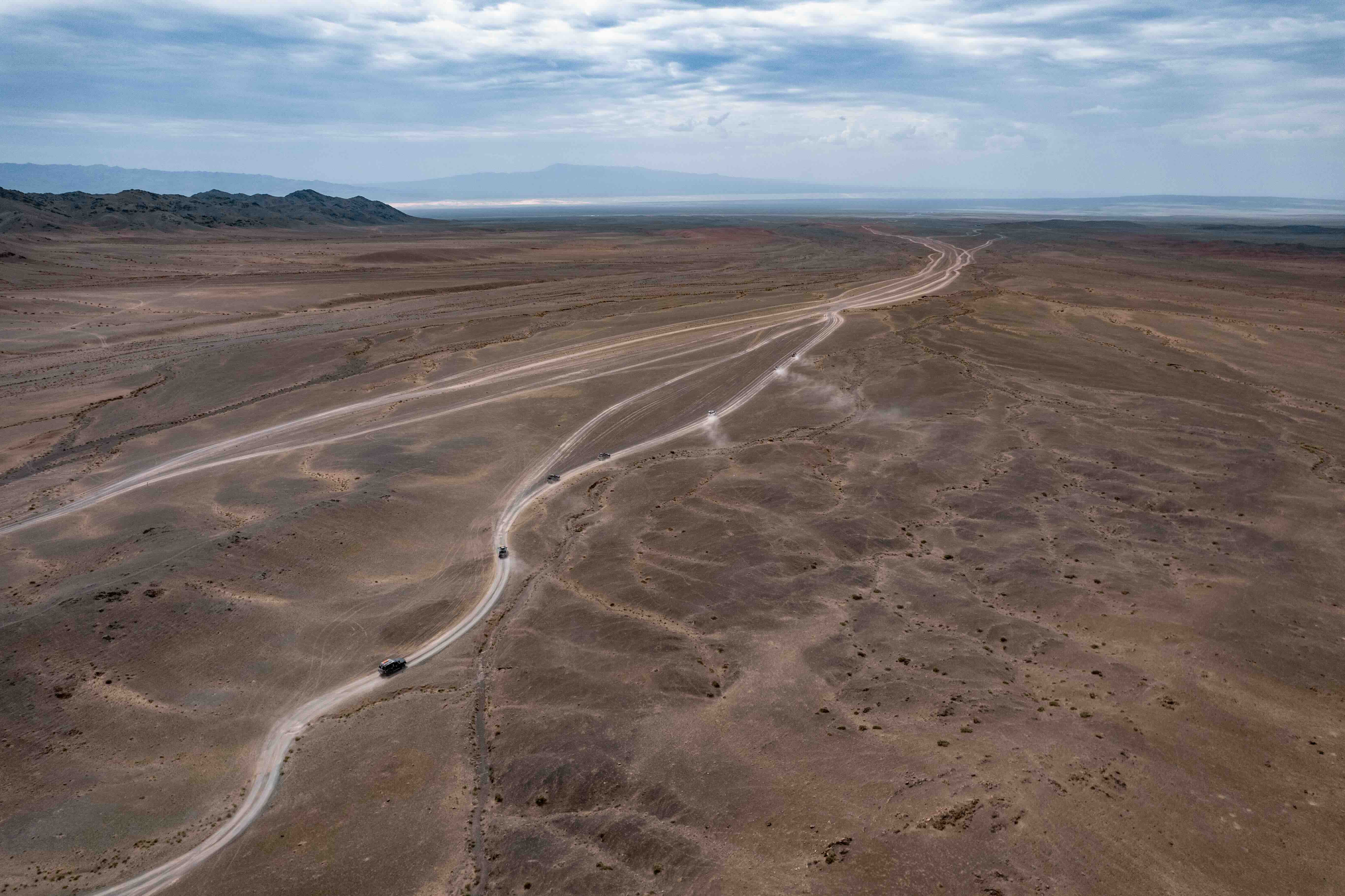 Aerial view of a vehicle convoy following winding tracks across flat desert terrain.
