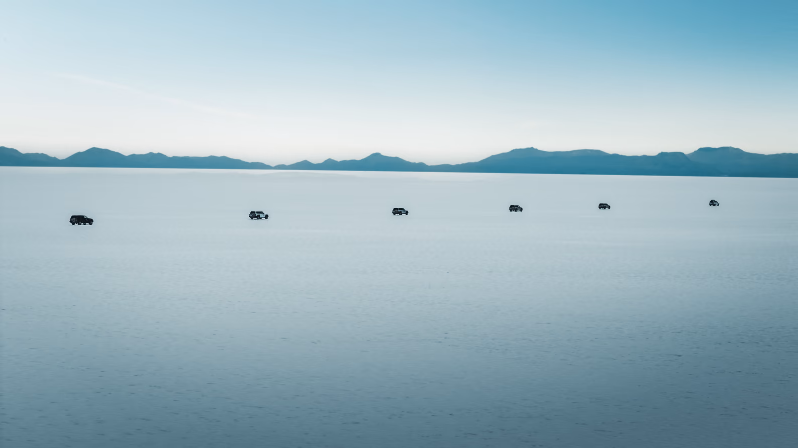 Seven 4WD vehicles crossing the Salar de Uyuni salt flats in Bolivia.