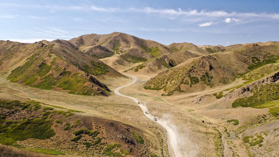 Two 4WD vehicles driving along a winding track through Mongolia’s Yol Valley.